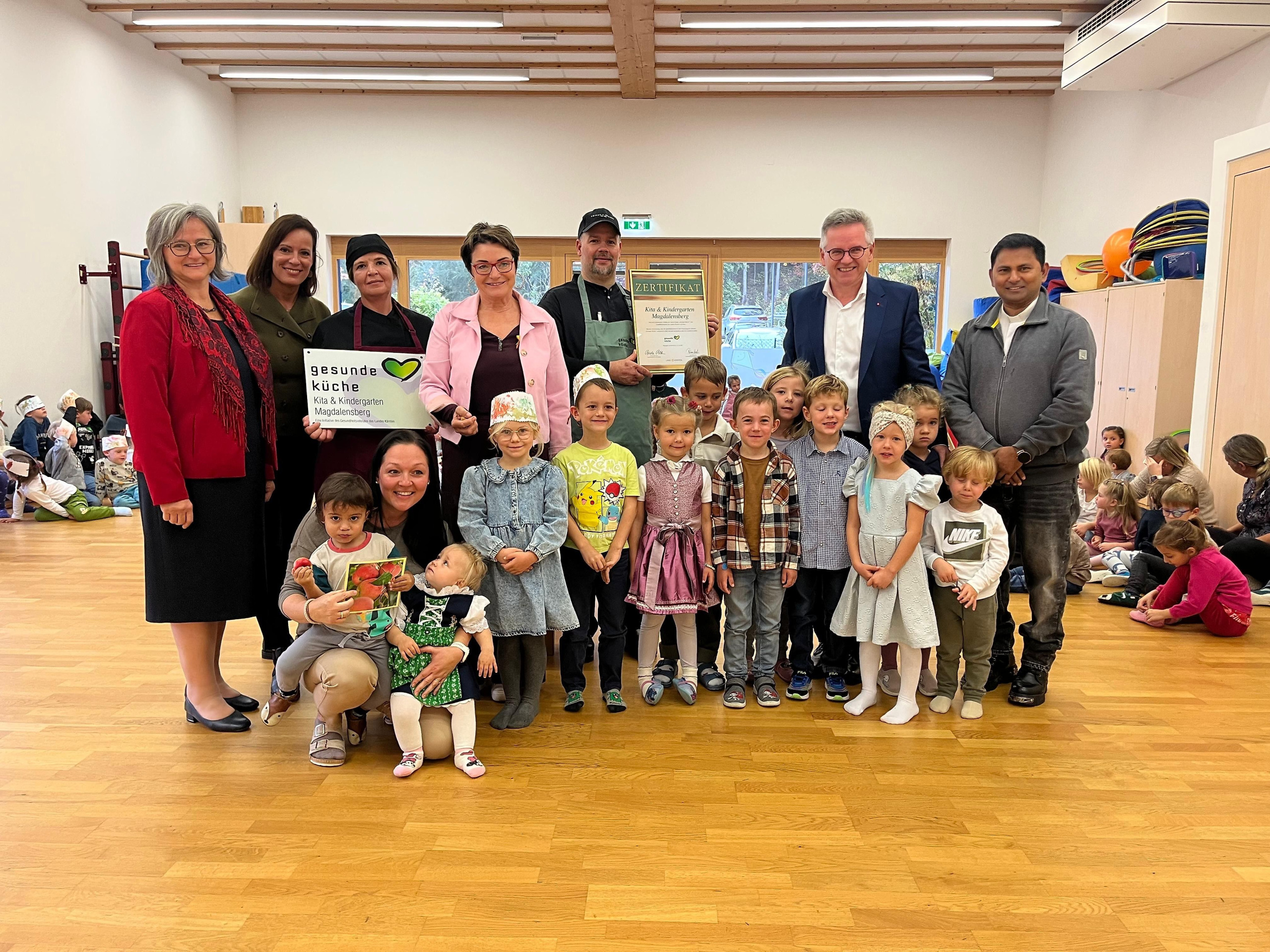 Kindergarten-Leiterin Marianne Kapelarie, Sonja Fidersek (Gesundheitsförderung, Land Kärnten), Isabella Hartl (Küchenteam), Landesrätin Beate Prettner, Küchenchef Jürgen Tomantschger, Bgm. Andreas Scherwitzl, Geist. Rat Pater Vijaya Madanu (von links) und vorne Claudia Pirker (KITA-Gruppenführung; vorne) mit Kindern
